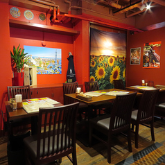 鮮やかなひまわりのタペストリーと、スペインの街並みを描いたアートが彩る明るい空間。壁際のテーブル席は、落ち着いて会話を楽しめる人気のお席です。