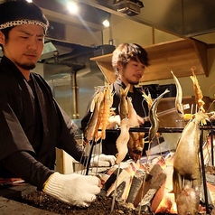 総席数112席の活気あふれる空間。カウンター席では、豪快な藁焼きや職人が焼き上げる原始焼きの臨場感あふれるパフォーマンスをお楽しみいただけます。お食事からご宴会まで幅広いシーンに対応可能です。※系列店舗の写真です。
