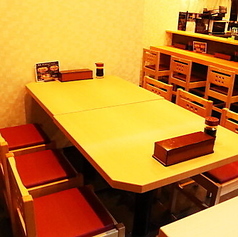 明るい木目を基調とした店内には、グループやご家族でのご利用に最適な広々としたテーブル席をご用意しております。快適な設計: 落ち着いたトーンの壁面と、赤色の座面がアクセントになった椅子が、リラックスできる空間を演出します。