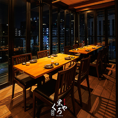 ［8～12名様］眼下に広がる景色と、温もりある木目のテーブルが織り成す上質な空間。ガラス張りの壁面が都会の煌めきを映し出し、洗練された静けさに包まれます。仲間と語らいの場に気品漂う設えです。