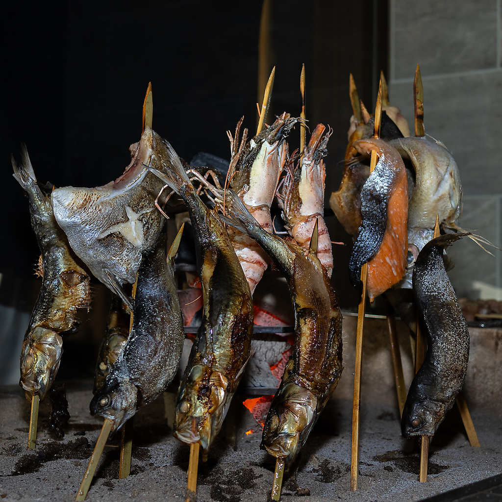 獲れたて鮮魚を囲炉裏で焼くように串焼きをする【名物　原始焼き】