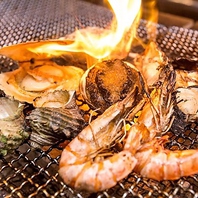 オープンキッチンで調理される新鮮な魚介や肉の炉端焼き