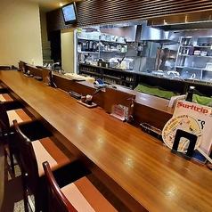 カウンター席は、木製の長いテーブルと背もたれ付きの椅子が並んでおり、調理場が見えるオープンキッチンスタイルです。[沼津/接待/蕎麦/手打ち/お酒/出張/個室]