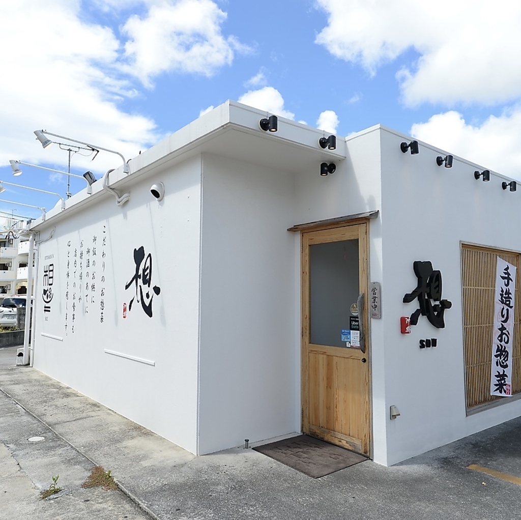 白壁に黒文字の看板が映える外観が特徴。沖縄市美原にある手作りお惣菜と和の空間で楽しむお店です。