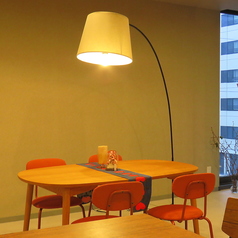 大きな弧を描くアームライトが主役の、デザイン性の高いテーブル席です。木のぬくもりを感じる楕円形のテーブルに、ポップなオレンジ色のチェアがアクセントを添えています。窓の外に見える無機質なビル群とは対照的に、室内には穏やかでクリエイティブな時間が流れています。