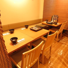 木の温もりに包まれた店内には、清潔感のある明るい色調のテーブル席が並びます。壁側はゆったりと寛げるベンチシートになっており、5名まで座れる広々としたスペースが魅力です。各席にコンロが完備され、落ち着いて食事を楽しめる空間です。