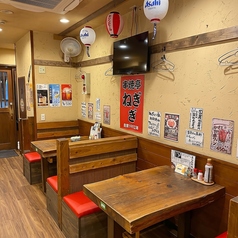 木目調のテーブルと赤い座面のシートが並ぶ、カジュアルなテーブル席エリアです。天井の提灯や壁掛けテレビが庶民的な居酒屋の雰囲気を演出し、少人数でも気軽に立ち寄って楽しめる居心地の良い空間です。