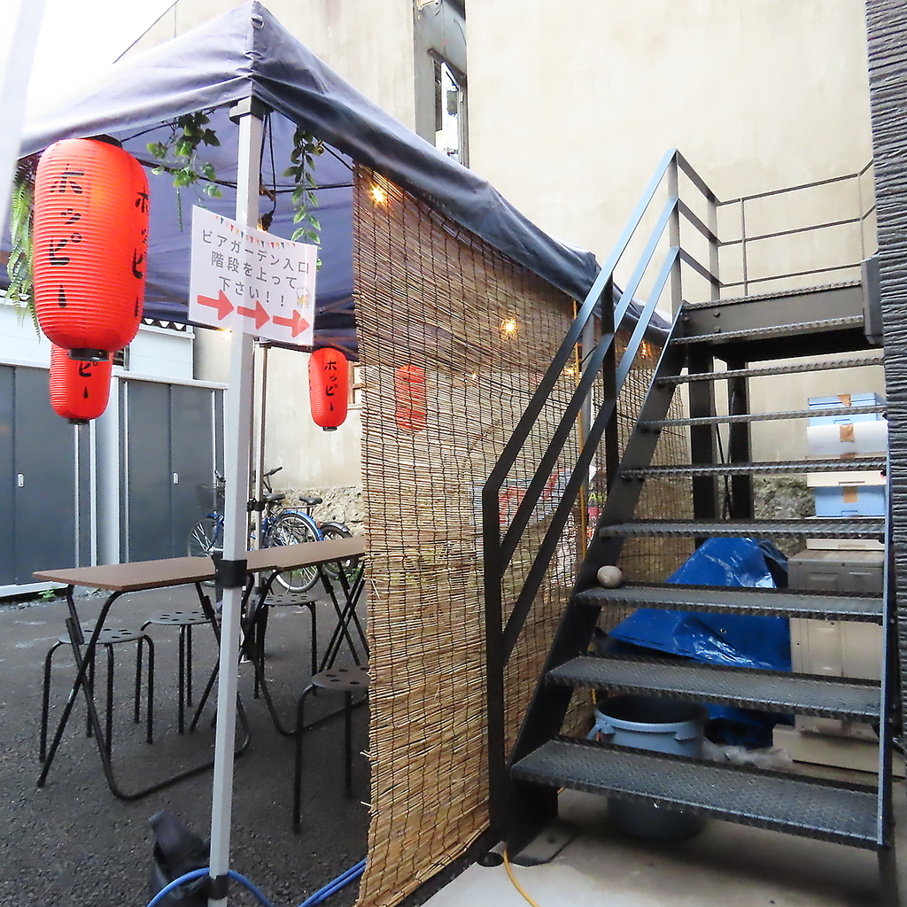 赤提灯が何ともエモい、ビアガーデンの入り口です。階段上がったその先に開放的な空間が広がります。