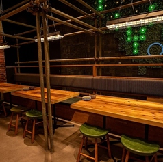 木のぬくもりあふれるテーブルと、深いグリーンのスツールが落ち着いた雰囲気を演出します。壁面には緑の装飾とネオンが灯り、都会的でスタイリッシュな印象。仲間と囲む食事やカジュアルな飲み会にもぴったりな、居心地の良い一角です。
