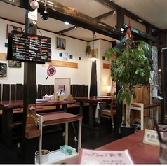 木の温もりに包まれた店内には、重厚感のある一枚板風のテーブル席が並びます。壁側はベンチシートになっており、グループでもゆったりと過ごせるのが魅力です。手書きのメニューボードや観葉植物が、アットホームで落ち着いた雰囲気を演出しています。