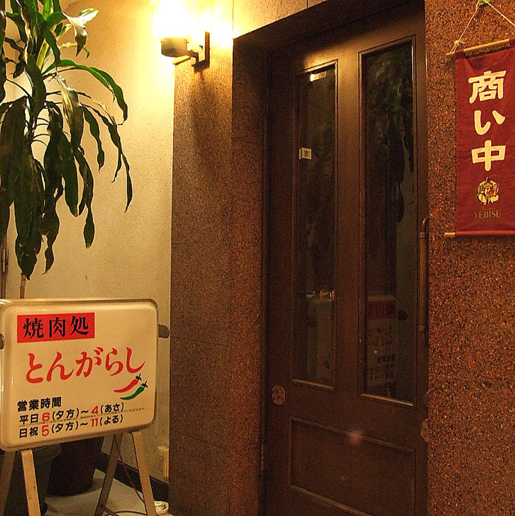 ビルの2Fにあるお店です。階段を上がって右側に焼肉処とんがらしが御座います。