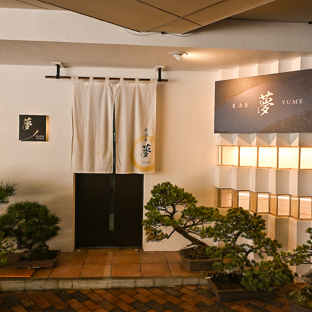 居酒屋「夢」で至福のひと時を。落ち着いた店構えと立派な盆栽が、大人の隠れ家へと優しく誘います。