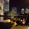 ブラックとウッドのコントラストが効いたスタイリッシュなテーブル席。昼は陽射しが降り注ぎ、夜は街の光と風が心地よく、いつの時間帯でも映えるスポット。空を眺めながら語らうひとときに、BBQの香りが彩りを添えてくれます。