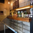 【立ち飲みカウンター席】無機質なコンクリートと温かな照明が調和する立ち飲みカウンター。ライブ感溢れる空間で、サクッと一杯楽しむのに最適です。