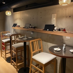 コンクリート壁と木の温もりが調和した、落ち着いた雰囲気のテーブル席。ほどよい高さのハイチェアは座り心地がよく、少人数での一杯にも最適です。控えめな照明が空間を柔らかく包み、静かに語り合える大人の時間を演出。調味料やメニューが整然と並び、気軽に入りやすい居心地の良さが感じられる一角です。