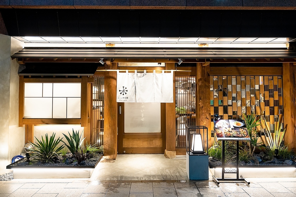 都会の喧騒に表れたモダン和風の趣ある外観。わずかな緑のはえる。