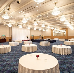 大宴会場全スパンを利用した立食パーティーの一例です。中央にビュッフェ台をゆったり配置し、天井高の空間に輝くシャンデリアが上質な雰囲気を演出。地元食材や旬の味覚を取り入れた料理も好評です。ステージや装花にも対応し、方針発表会や懇親会、お祝い会、お別れの会など幅広い用途でご利用いただけます。