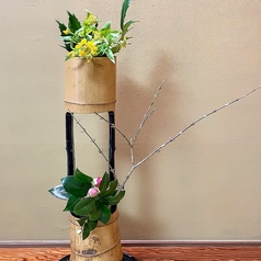 竹の花器に菜の花、レンギヨウの枝に2種の椿。