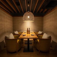 木目の美しいテーブルと椅子、シンプルながらも洗練された空間。木のパーテーションで緩やかに区切られており、周囲を気にせず会話を楽しめる落ち着いた雰囲気。暖色系の照明が、天然木の質感を際立たせ、和の安らぎを与えています。プライベートな食事や、ビジネスシーンでの利用にも最適な、大人のための居酒屋