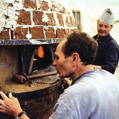 ナポリの窯職人が作ったピザ釜で焼き上げます機械式ではなく、原始的な耐火レンガを使用した窯だからこそ、再現できる450°c～500°cという火力。本場イタリア・ナポリで数々の窯を生んできた伝統の技で、ここ名古屋の地にそれを再現しました。(写真：窯作りの様子)