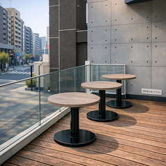 建物沿いに設けたテラス席は、街の空気を身近に感じられる心地よいスペース。木目調の床とシンプルなテーブルが、都会的で洗練された印象を演出します。周囲を見渡しながら、昼はカジュアルに、夜は落ち着いて過ごせる特別感のある席で、気軽な食事や一杯にも最適です。