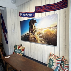 【開放感あふれるカジュアルテラス席】白木の壁に映える迫力の犬のフォトアートと、ポップなクッションが目を引く3名用のテラス席。リゾート感と遊び心を兼ね備えた空間で、ゆったりとした時間を楽しめます。友人とのカジュアルな食事や気軽な集まりにもおすすめの寛ぎスポットです。